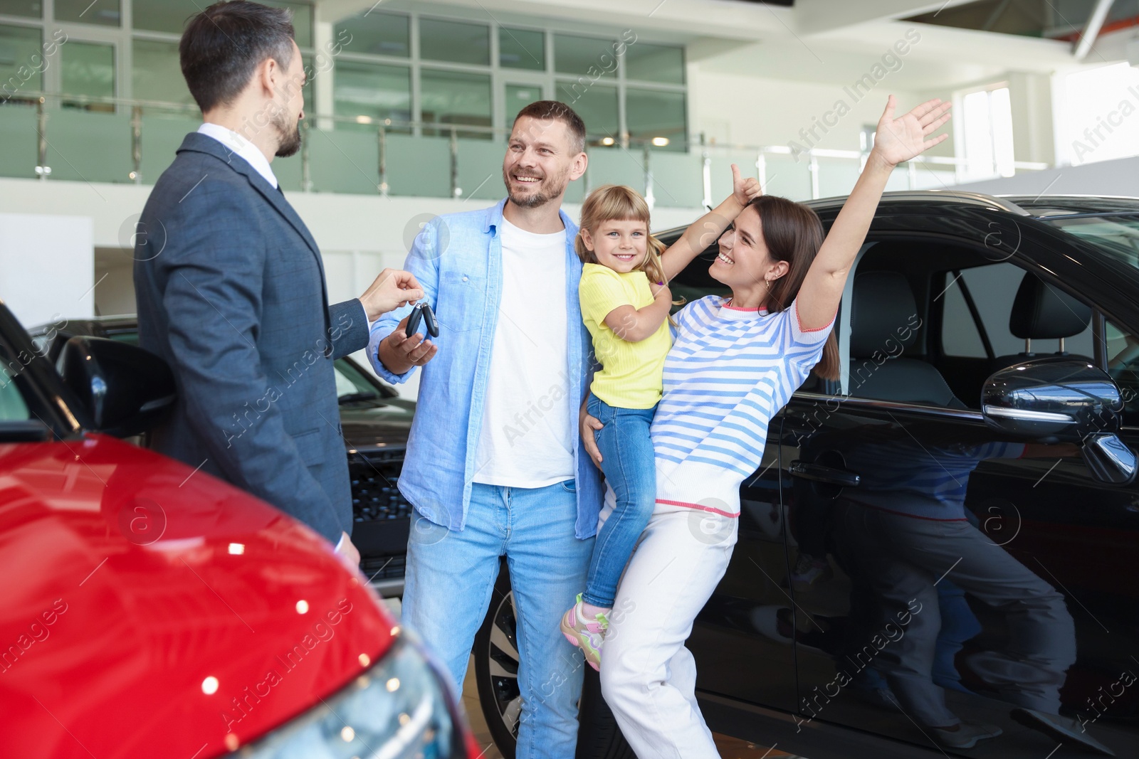Photo of Salesman giving car key to happy family in salon