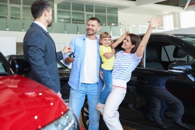 Photo of Salesman giving car key to happy family in salon