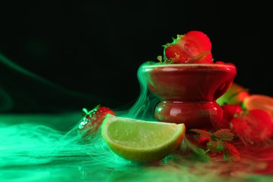 Photo of Hookah bowl with limes, strawberries, mint and smoke on black table, closeup. Space for text