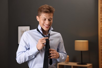 Photo of Man tying stylish black necktie at home