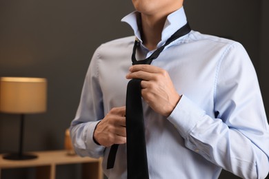 Photo of Man tying stylish necktie at home, closeup
