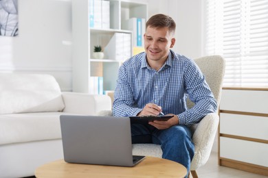 Photo of Smiling psychologist with clipboard during online session by laptop in office