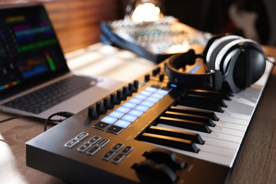 Photo of MIDI keyboard with headphones, laptop and dj mixer on wooden table indoors, closeup
