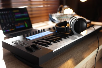 Photo of MIDI keyboard with headphones, laptop and dj mixer on wooden table indoors, closeup