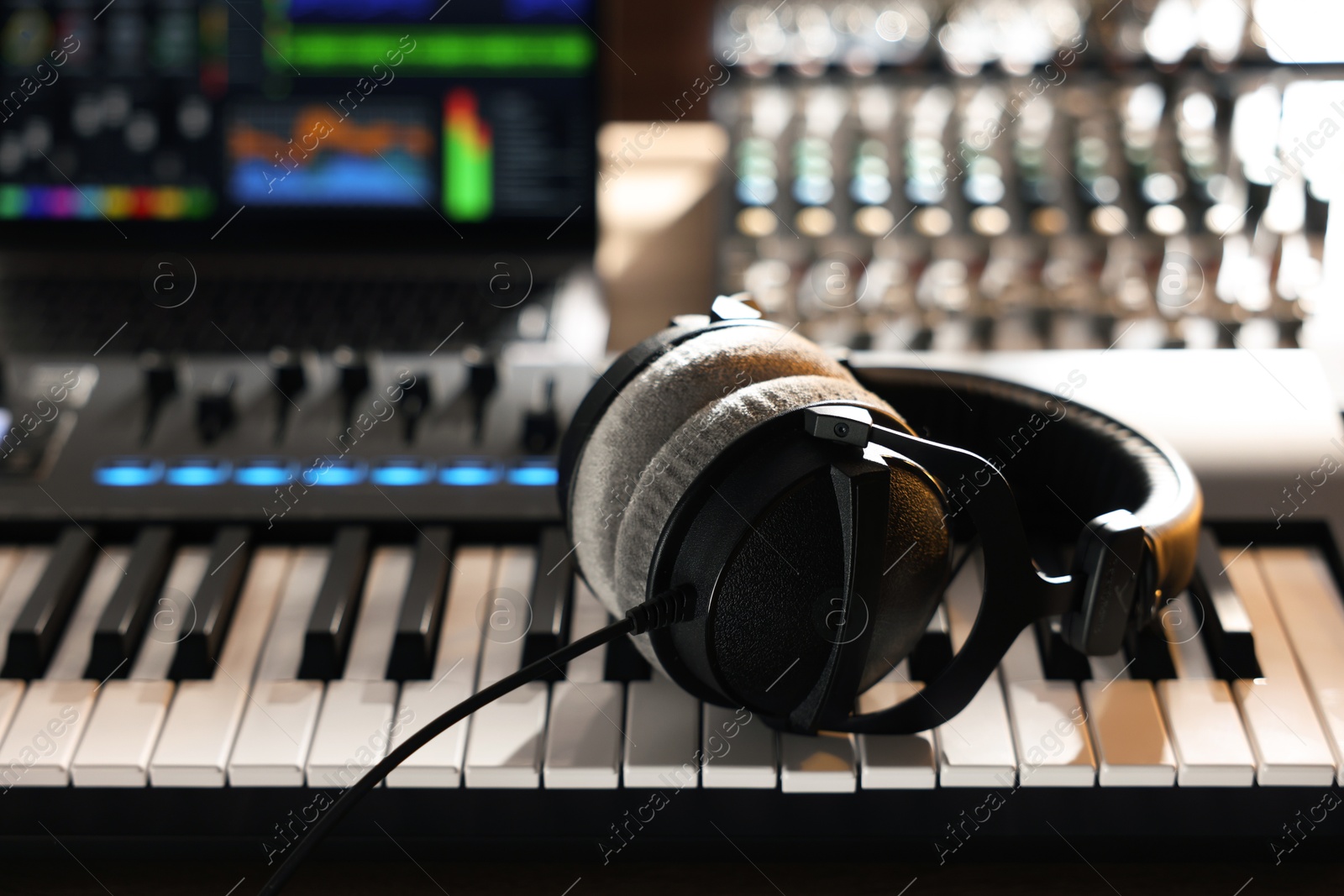 Photo of MIDI keyboard with headphones, dj mixer and laptop on table, closeup