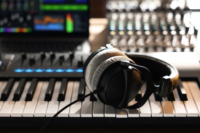Photo of MIDI keyboard with headphones, dj mixer and laptop on table, closeup