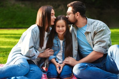 Photo of Family portrait of parents kissing their happy daughter in park