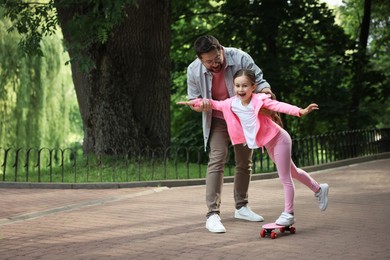 Photo of Family getaway. Happy father and daughter having fun with penny board in park. Space for text