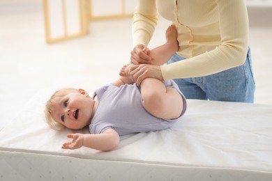 Photo of Mother playing with her cute baby on changing table at home, closeup