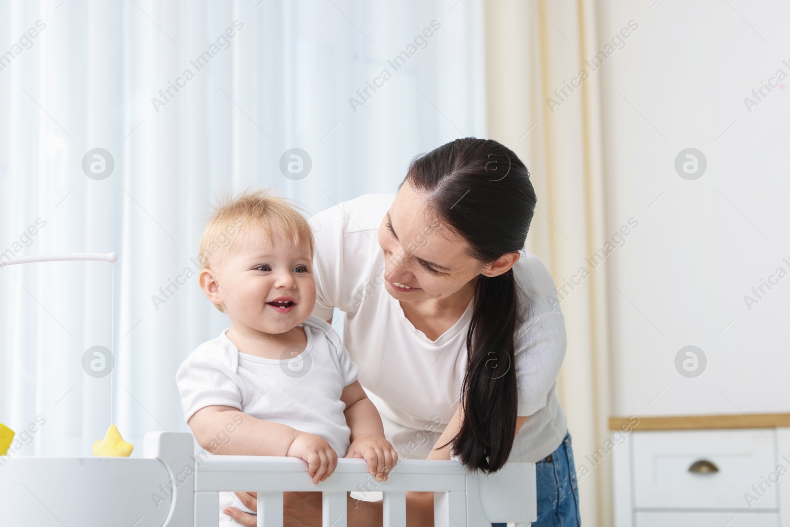 Mother playing with her cute baby in crib at home Photo of Mother playing with her cute baby in crib at home