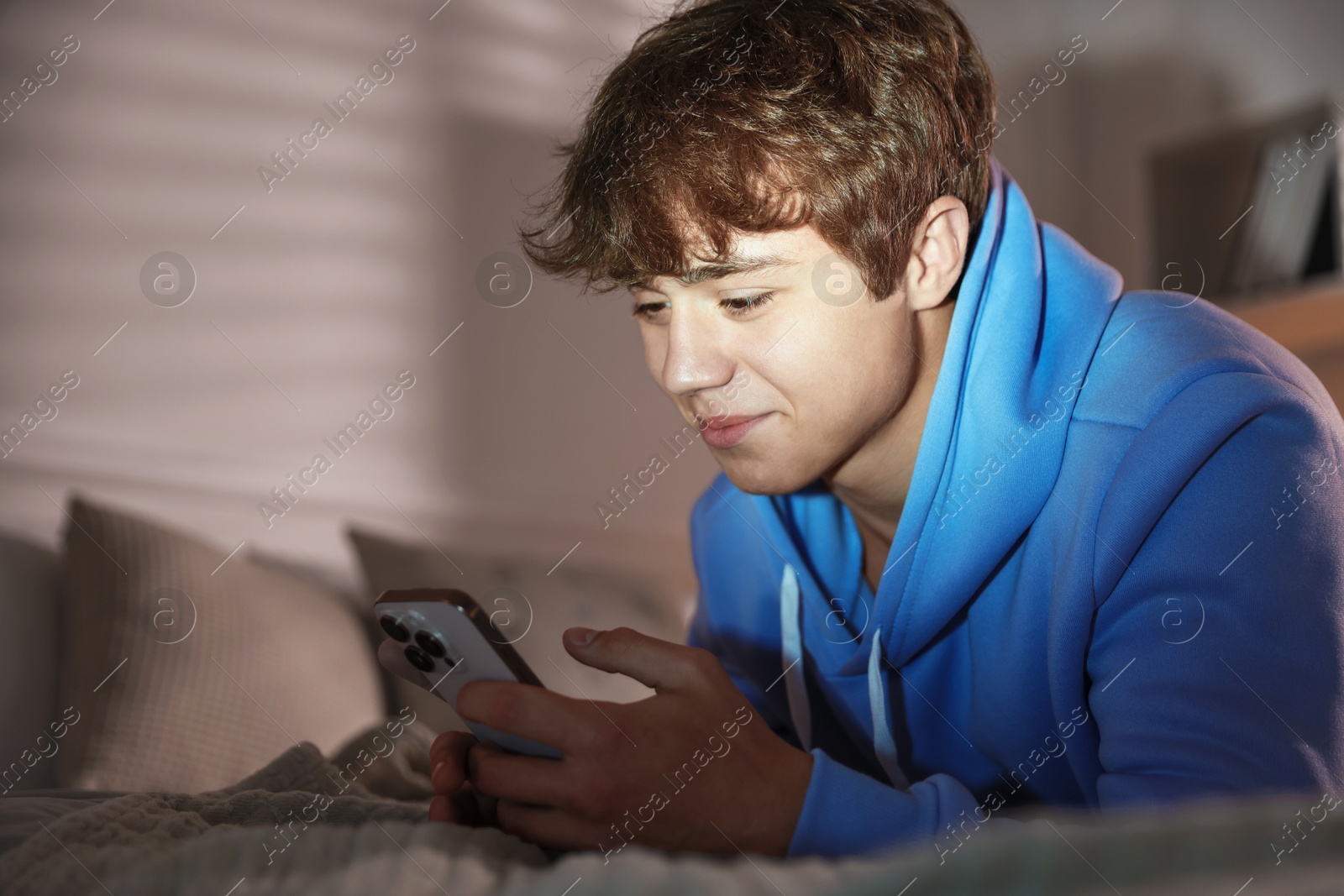 Photo of Teenage boy using smartphone on bed at home. Space for text