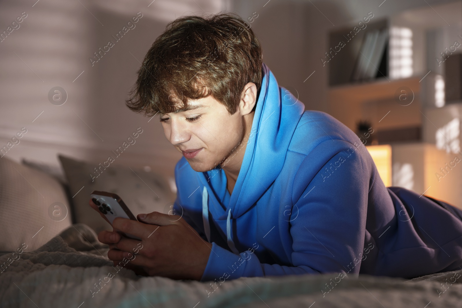 Teenage boy using smartphone on bed at home Photo of Teenage boy using smartphone on bed at home