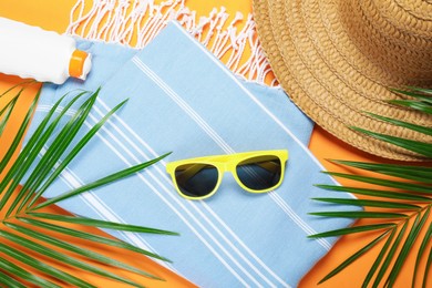 Photo of Beach accessories and palm leaves on orange background, flat lay