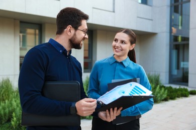Photo of Happy coworkers discussing something near office building