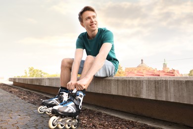 Photo of Happy man putting on roller skates outdoors