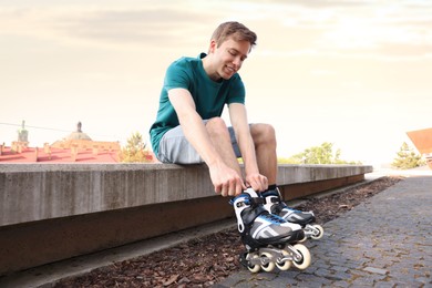 Photo of Happy man putting on roller skates outdoors