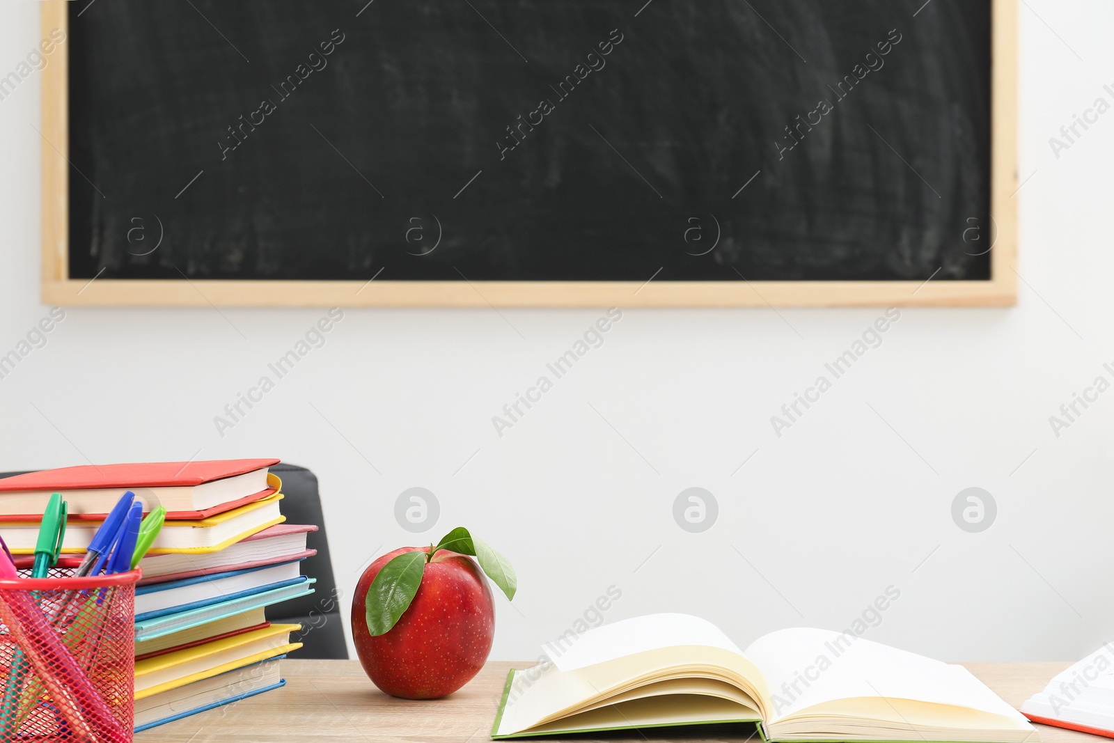 Different stationery and red apple on wooden table near blackboard indoors, closeup Photo of Different stationery and red apple on wooden table near blackboard indoors, closeup
