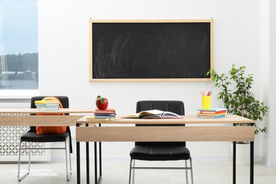 Photo of Different stationery and red apple on wooden table near blackboard indoors