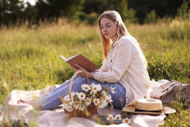 Photo of Beautiful woman with bouquet of wildflowers reading book on blanket in meadow