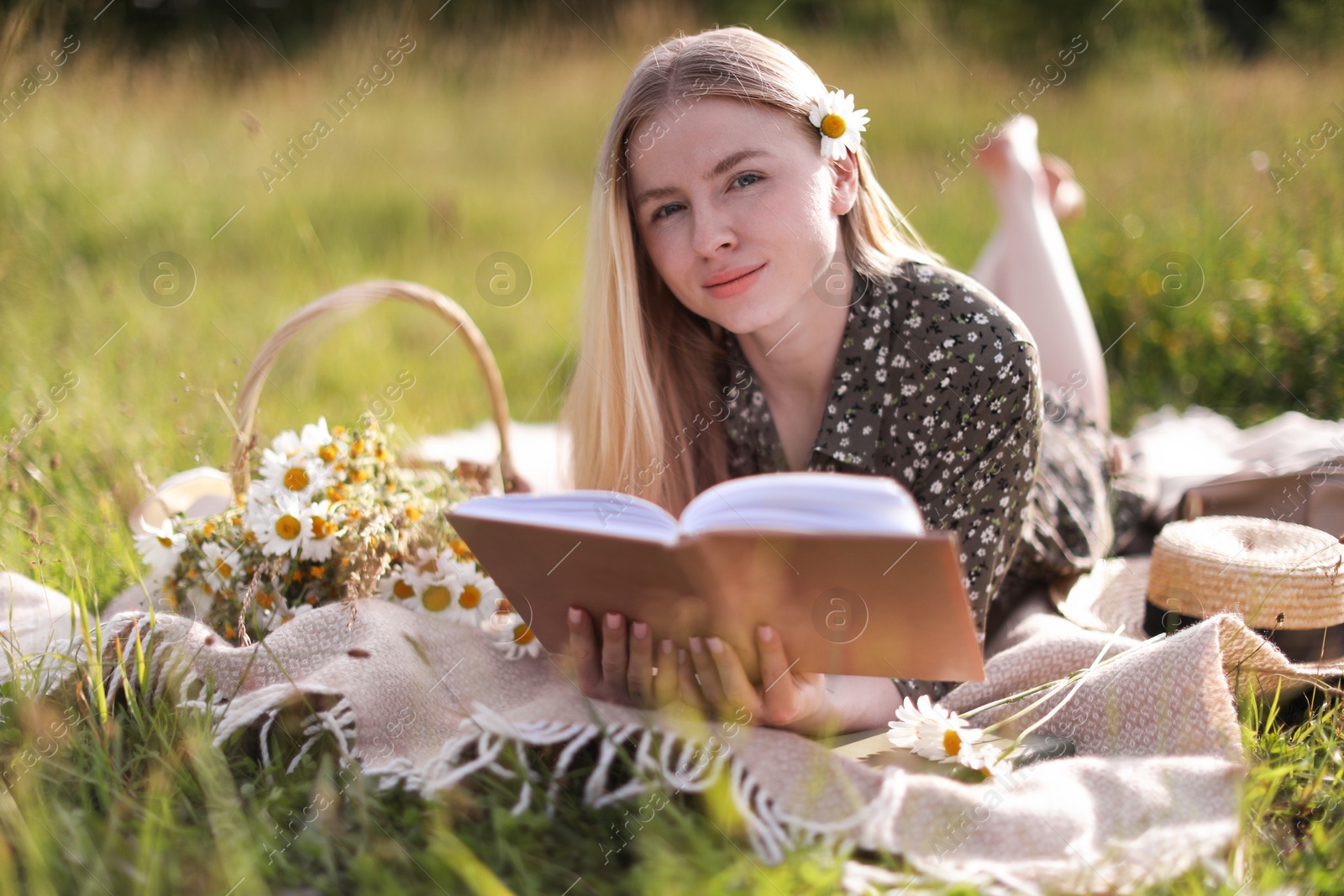 Beautiful woman with bouquet of wildflowers reading book on blanket in meadow Photo of Beautiful woman with bouquet of wildflowers reading book on blanket in meadow