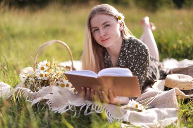 Photo of Beautiful woman with bouquet of wildflowers reading book on blanket in meadow