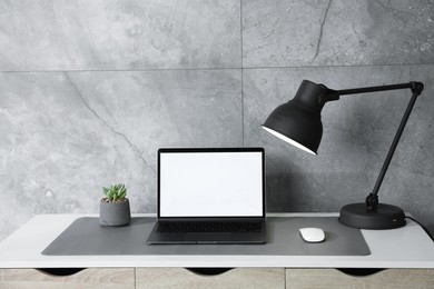 Photo of Stylish workplace with laptop and grey mousepad on white table indoors. Space for text