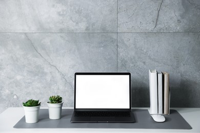 Photo of Stylish workplace with laptop and grey mousepad on white table indoors. Space for text