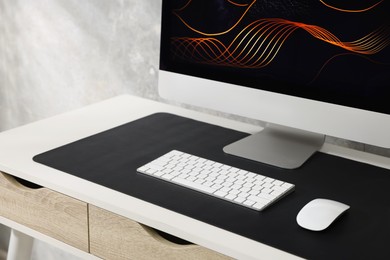 Photo of Stylish workplace with computer and black mousepad on white table indoors, closeup