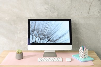 Photo of Stylish workplace with computer and pink mousepad on wooden table indoors