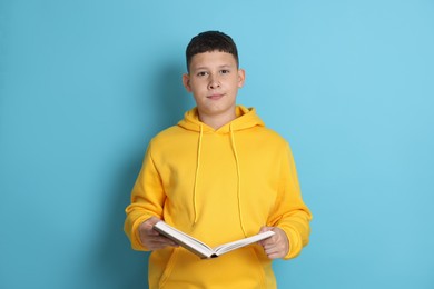 Photo of Teenage boy reading book on light blue background