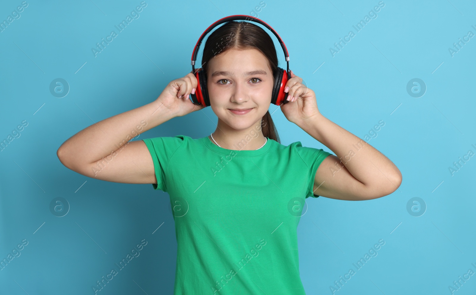 Teenage girl in headphones on light blue background Photo of Teenage girl in headphones on light blue background