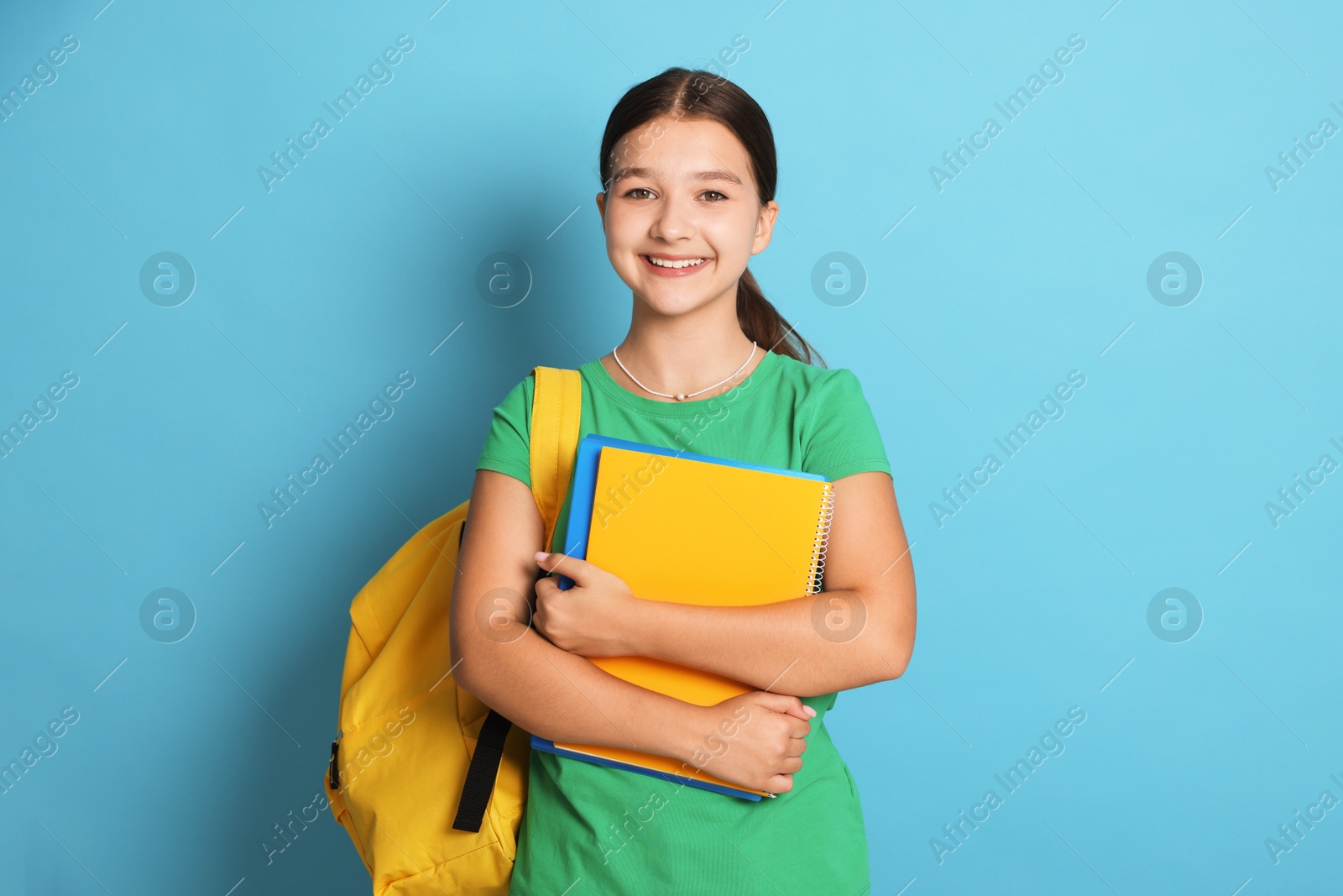 Teenage girl with backpack and notebooks on light blue background Photo of Teenage girl with backpack and notebooks on light blue background