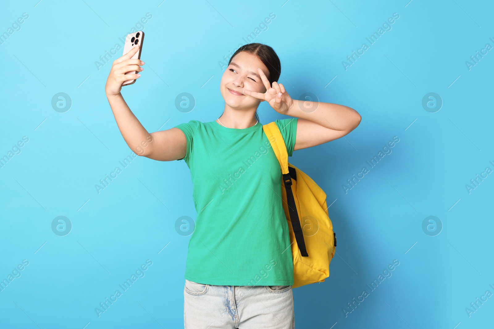 Teenage girl with backpack taking selfie on light blue background Photo of Teenage girl with backpack taking selfie on light blue background