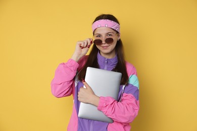 Photo of Teenage girl in sunglasses with laptop on yellow background