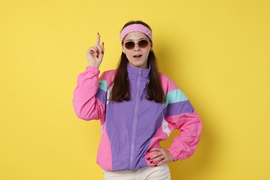 Photo of Teenage girl in sunglasses pointing at something on yellow background