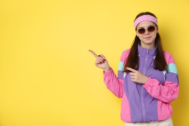 Photo of Teenage girl in sunglasses pointing at something on yellow background, space for text