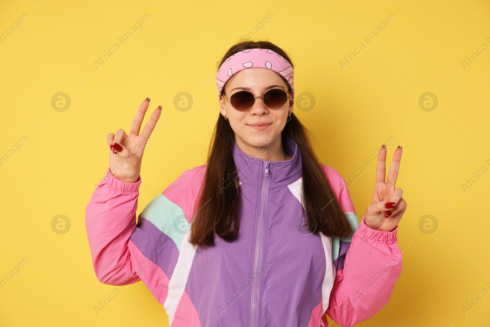 Teenage girl in sunglasses showing peace sign on yellow background Photo of Teenage girl in sunglasses showing peace sign on yellow background