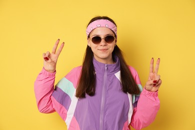 Photo of Teenage girl in sunglasses showing peace sign on yellow background