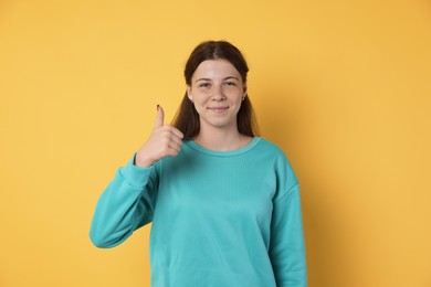 Photo of Teenage girl showing thumbs up on yellow background