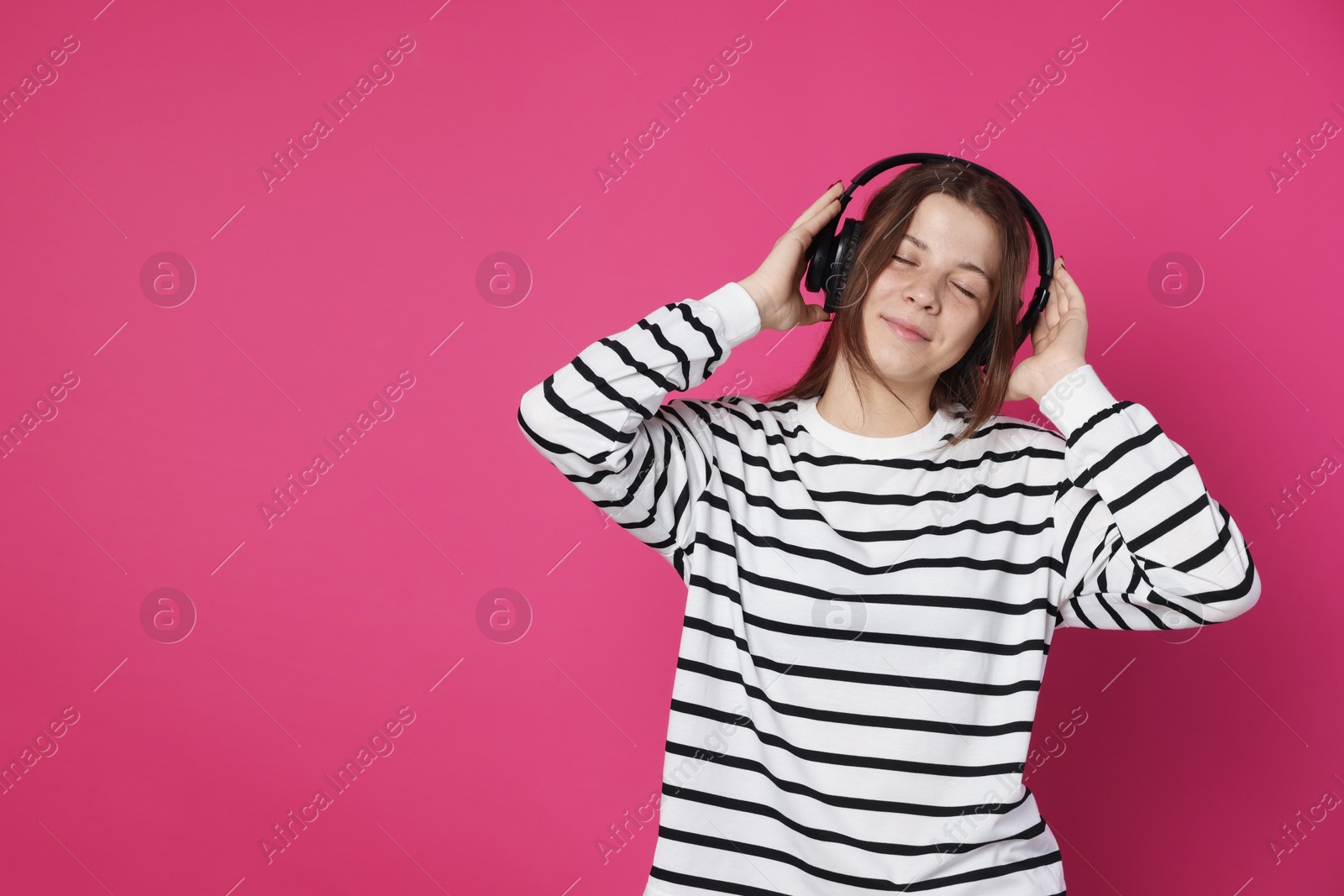 Teenage girl in headphones on crimson background, space for text Photo of Teenage girl in headphones on crimson background, space for text