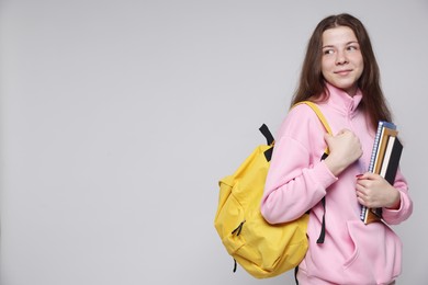 Photo of Teenage girl with backpack and notebooks on light grey background, space for text