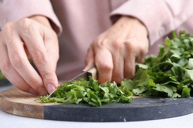 Photo of Woman cutting fresh green cilantro at light table, closeup