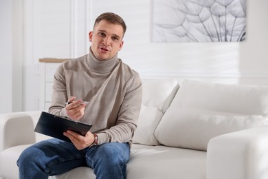 Photo of Psychologist with clipboard and pen talking during session on sofa in office