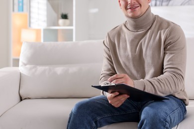 Photo of Smiling psychologist with clipboard on sofa in office, closeup. Space for text