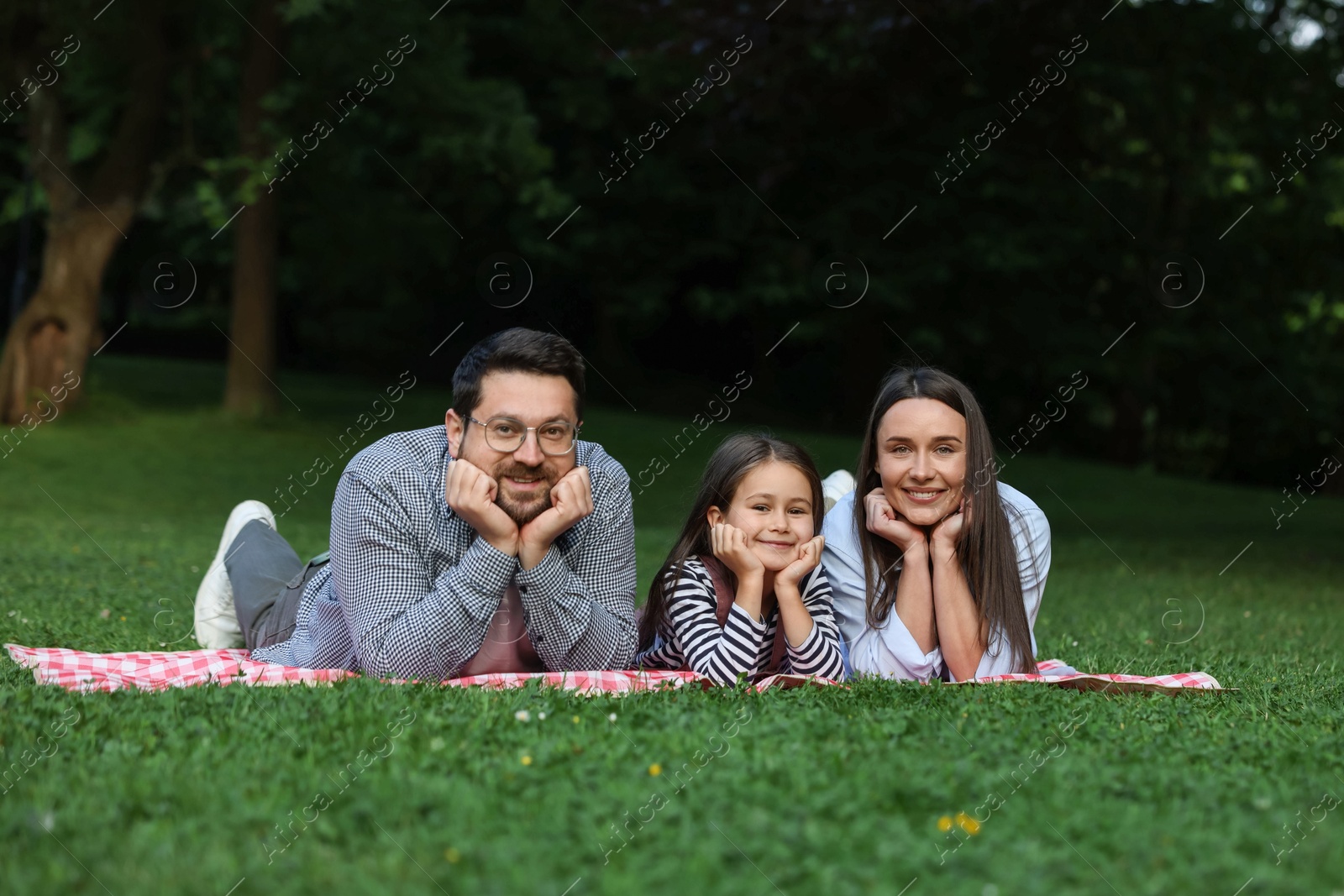 Photo of Happy family posing on checkered picnic blanket outdoors
