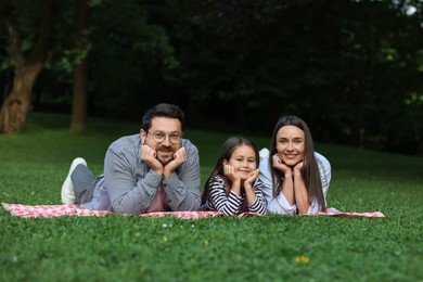 Photo of Happy family posing on checkered picnic blanket outdoors