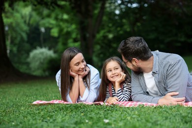 Photo of Happy family spending time together on checkered picnic blanket outdoors