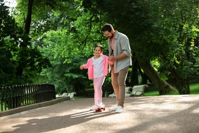 Photo of Family getaway. Happy father and daughter having fun with penny board in park