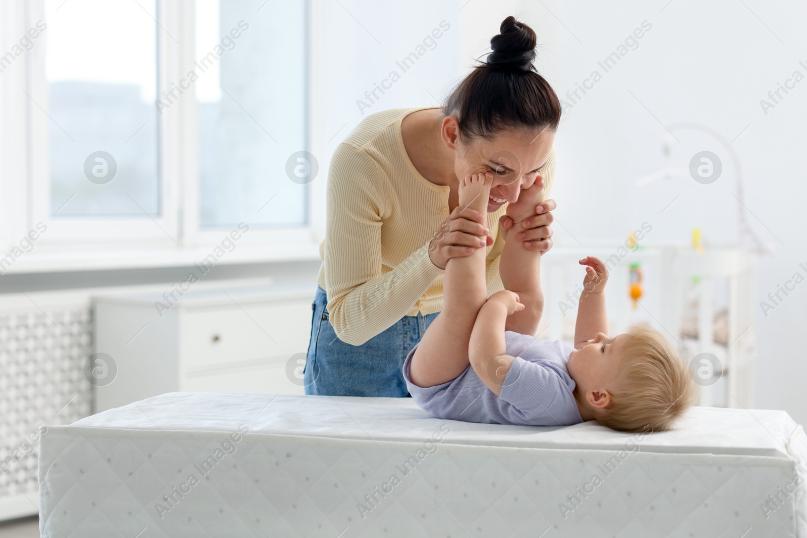 Photo of Mother playing with her cute baby on changing table at home