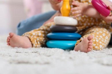 Photo of Mother and her little baby playing with toy pyramid on floor at home, closeup
